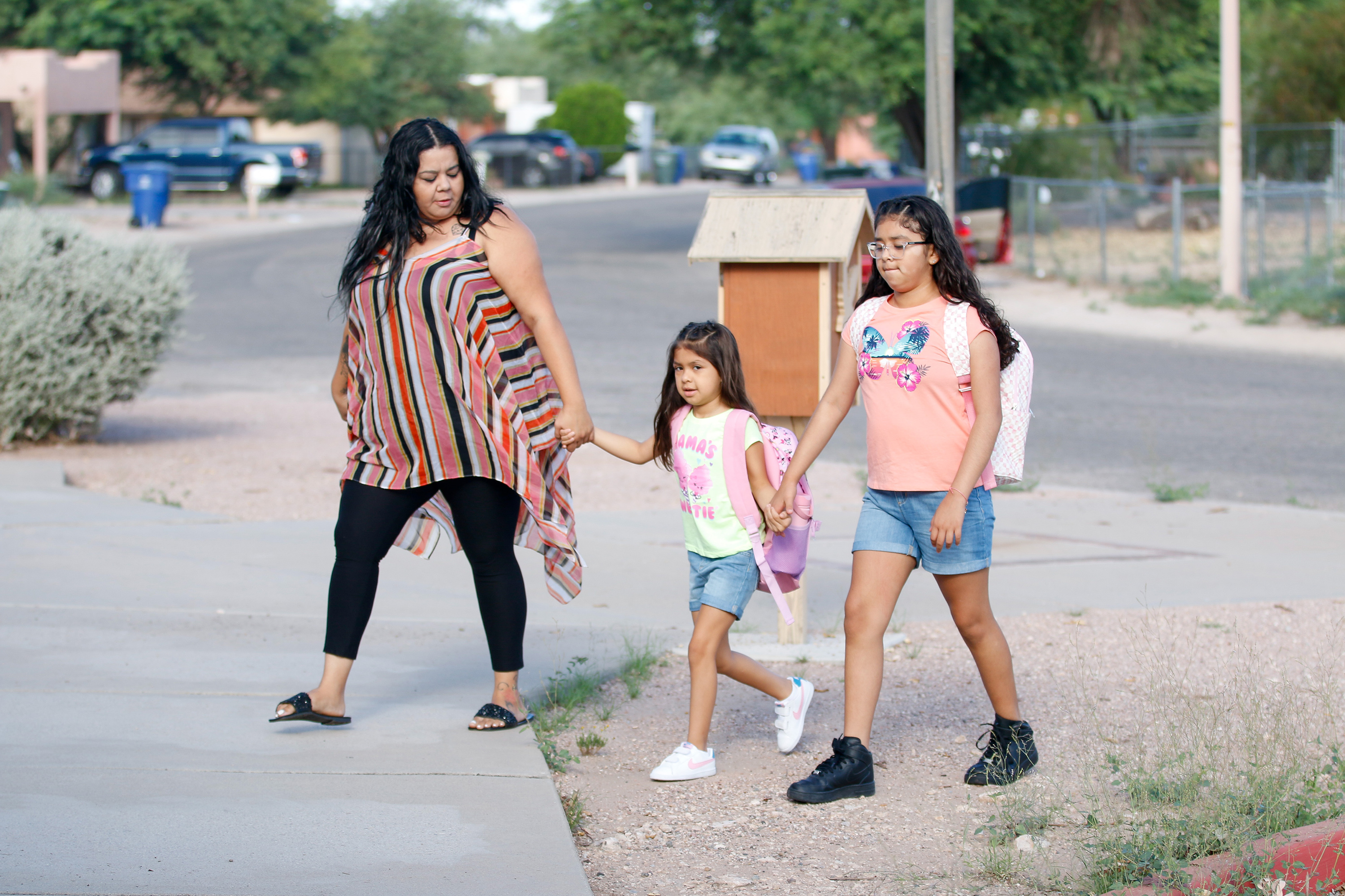 Two sisters and their mom hold hands while walking to school on the second day