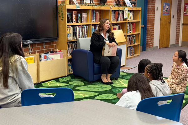 A woman holds books as she prepares to read to students sitting on the floor