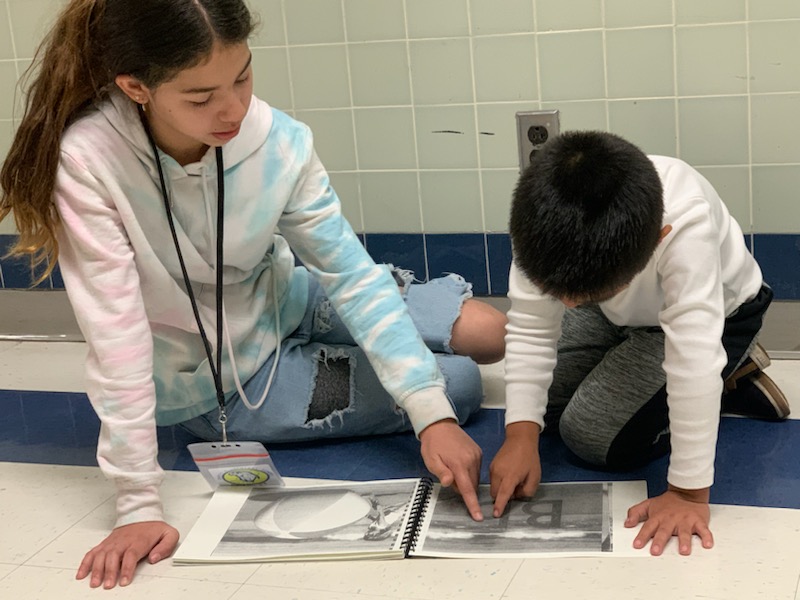 A 5th grade girl shows her kindergarten mentee a book