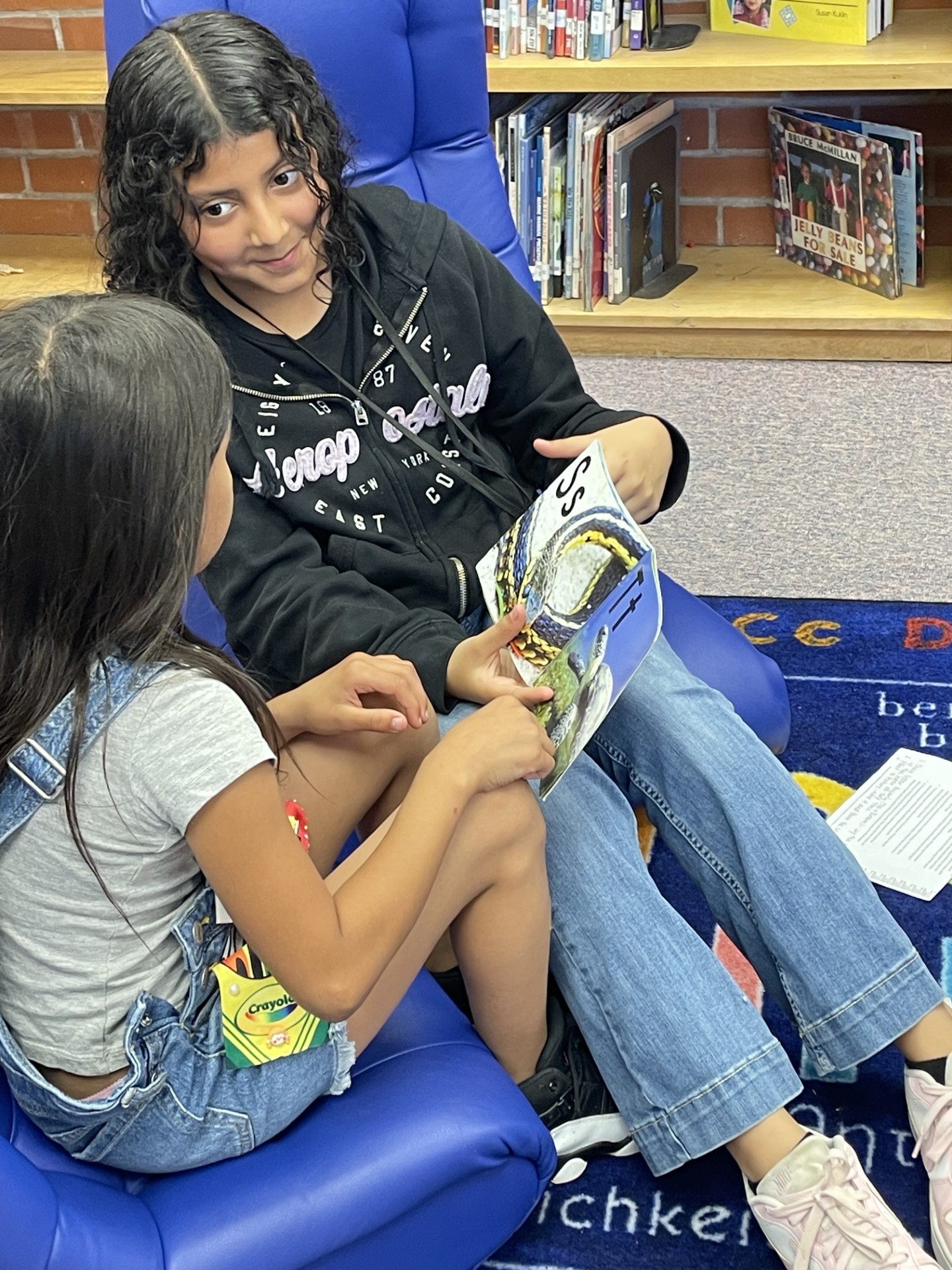 A 5th grade girl shows her kindergarten mentee letters in a book